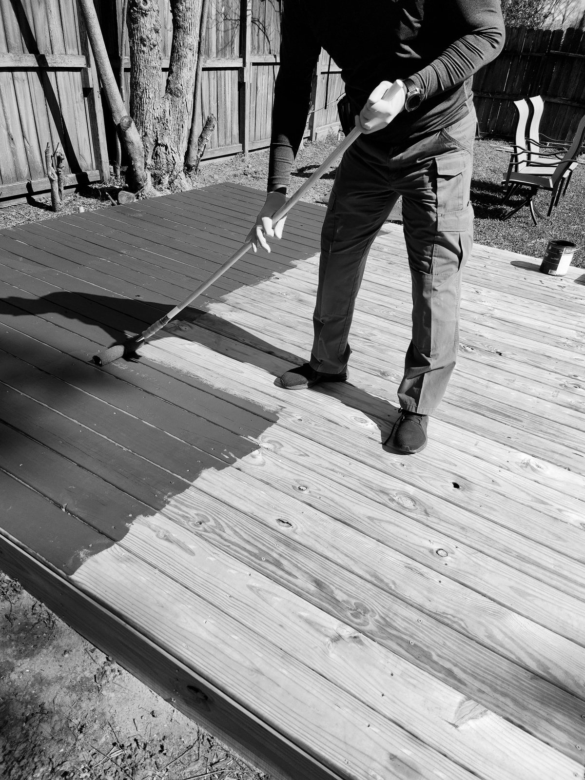 a person using a paint roller to paint a wooden deck